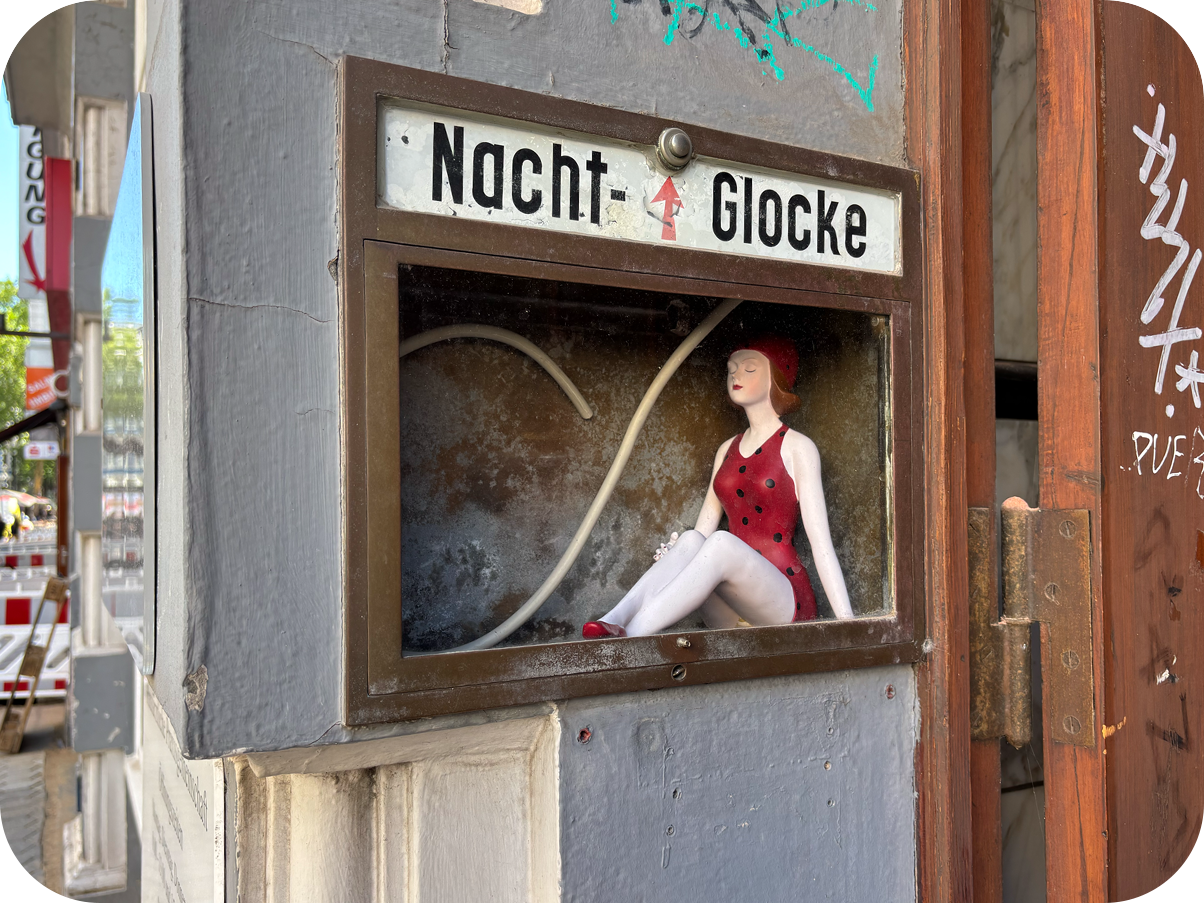 Schaukasten mit einer Frauenfigur und einem Klingelknopf neben dem Begriff „Nacht-Glocke“